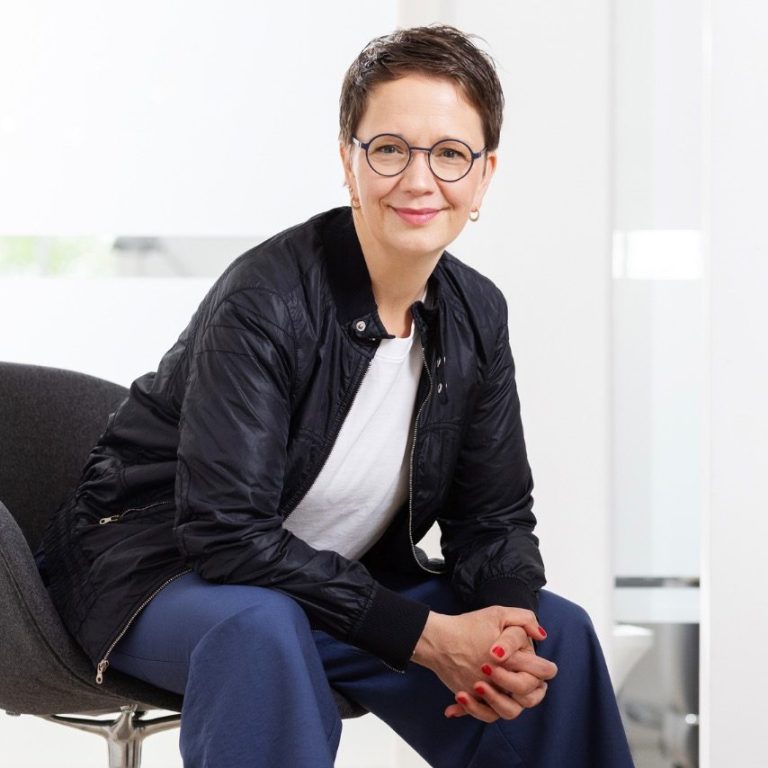 Anika Franke Das Bild zeigt Anika Franke, wie sie auf einem Stuhl sitzt und in die Kamera lächelt.